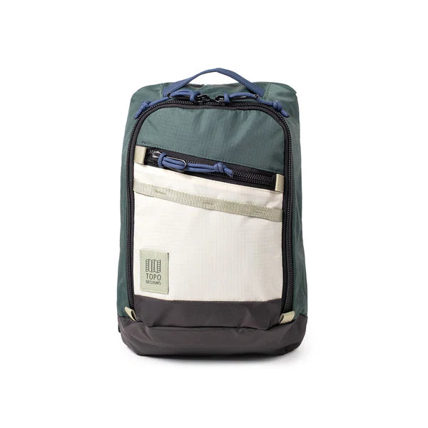 Colorblock sling bag with forest green top, cream bottom panel, and front zip pocket