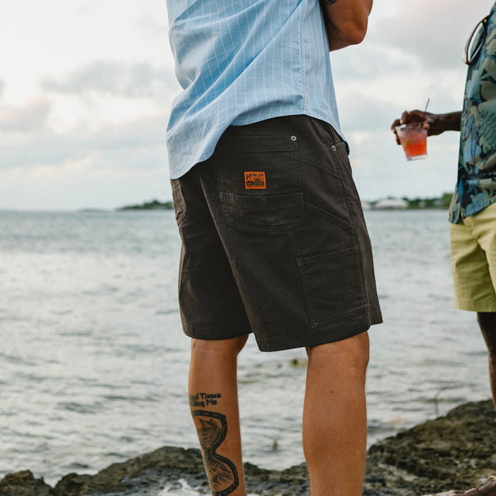 Dark olive canvas work shorts with multiple pockets worn by person at waterfront