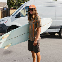 Man carrying surfboard wearing dark brown casual shorts in lifestyle setting