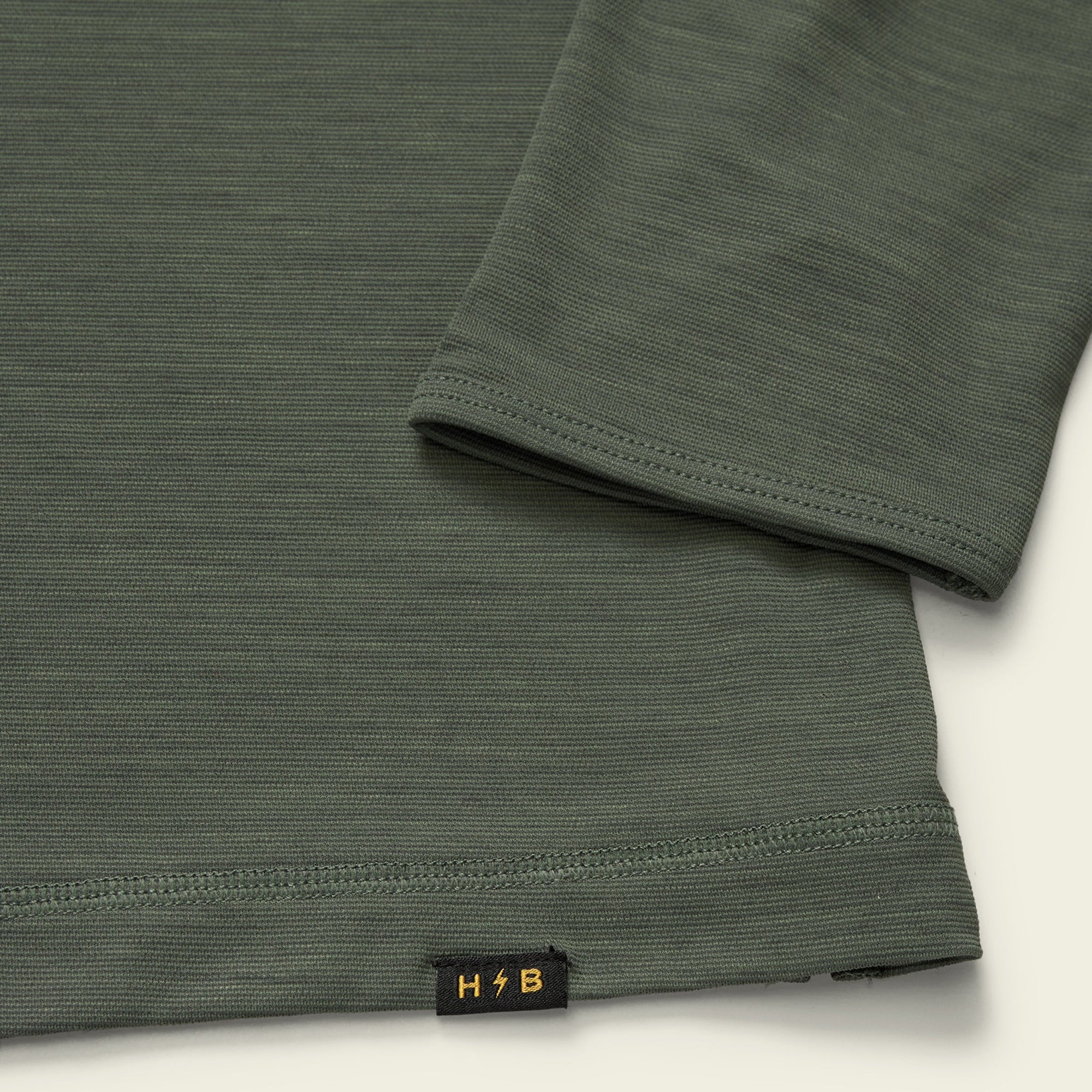 Olive green long sleeve hoodie detail showing sleeve cuff and hem with small logo tag