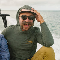 Man wearing olive green hooded long-sleeve tech shirt on boat with ocean background