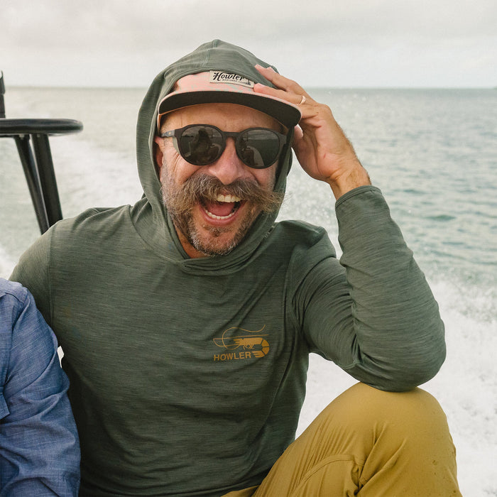 Man wearing olive green hooded long-sleeve tech shirt on boat with ocean background