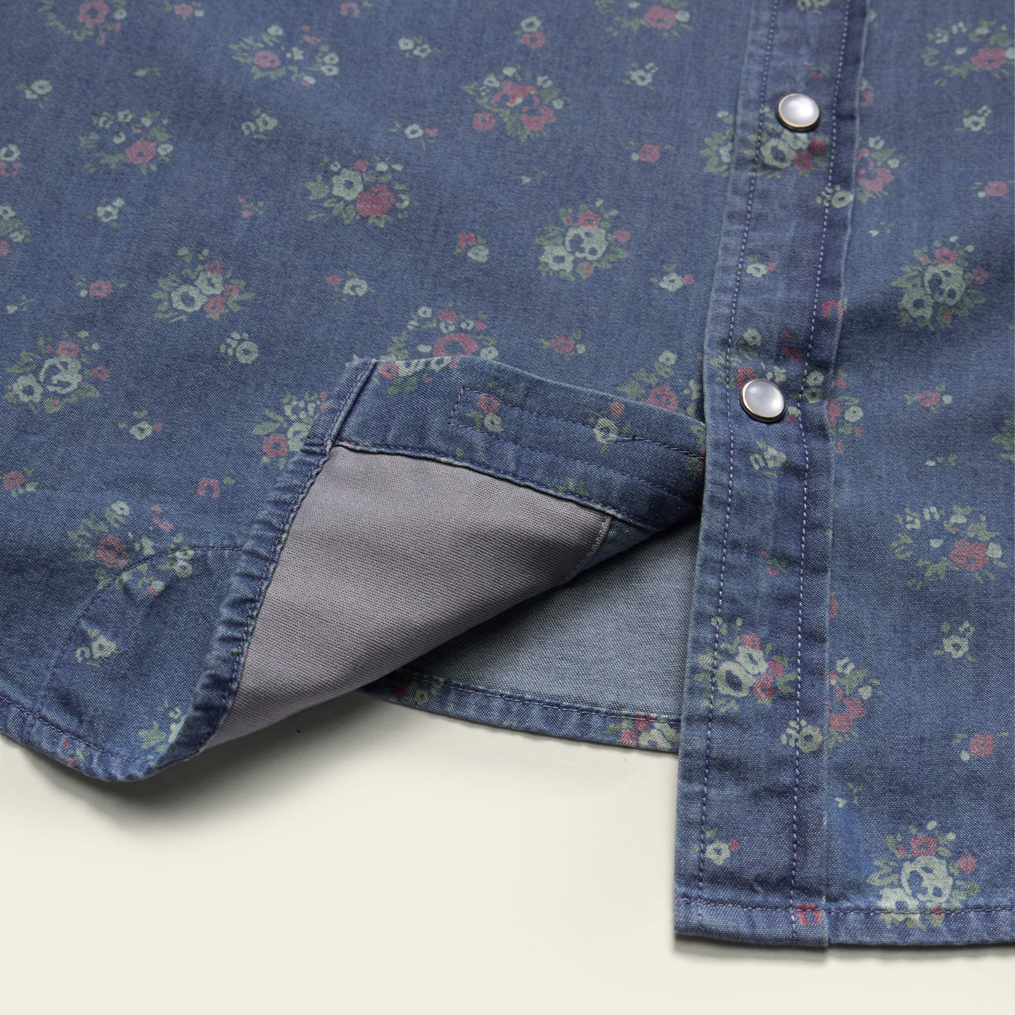 Close-up detail of floral print snap shirt hem and placket with silver snaps, showing lining