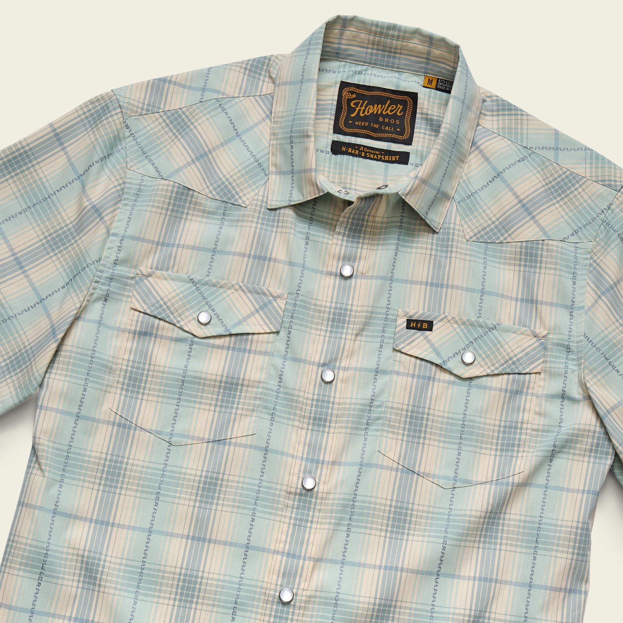 Men's short-sleeve western snap shirt in light seafoam plaid, angled flat-lay view showing chest pockets