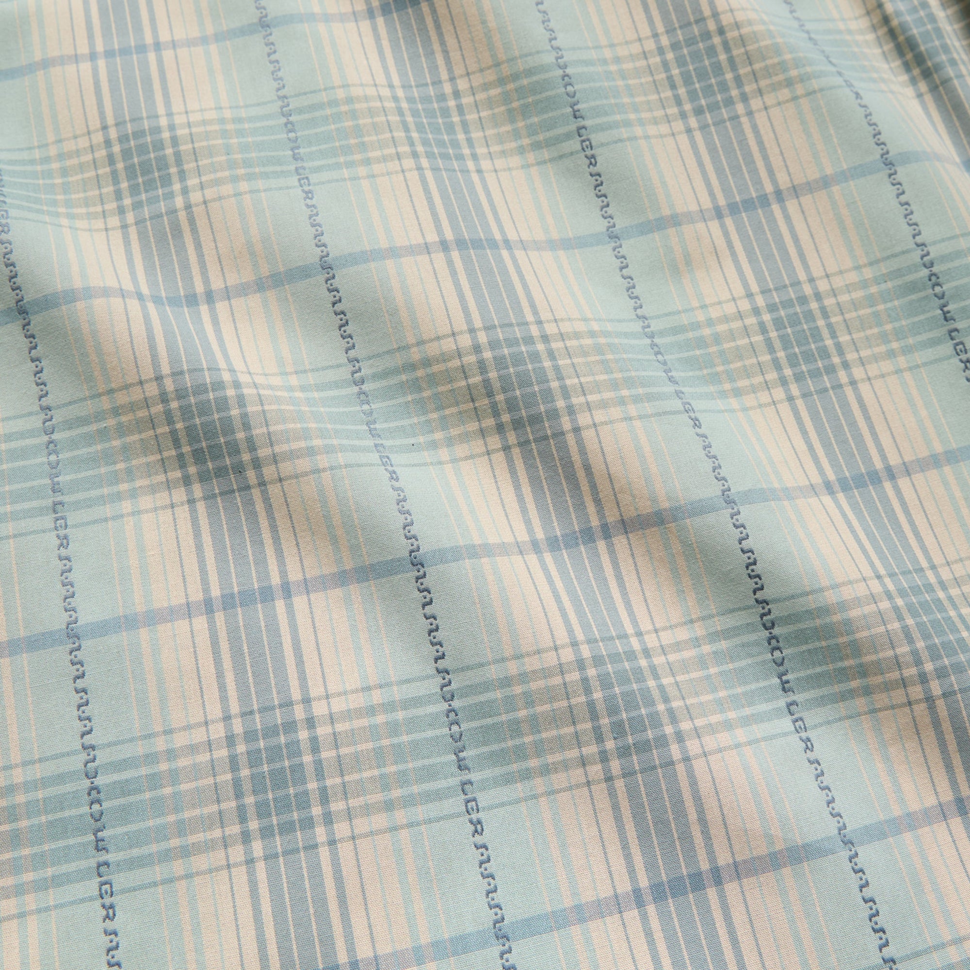 Close-up detail of plaid woven fabric with seafoam, beige, and blue tones and decorative stitching