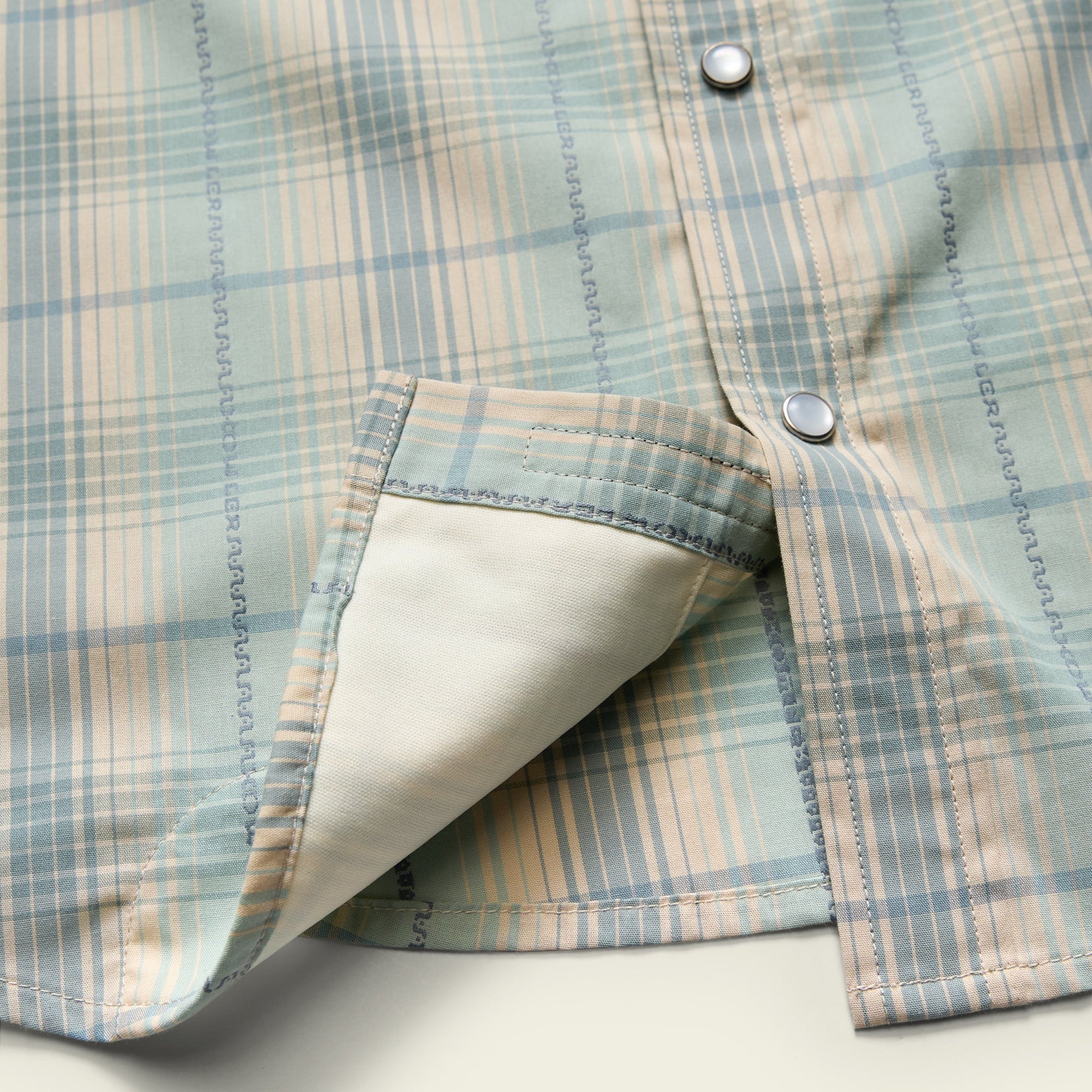 Close-up detail of plaid snap-button shirt hem folded back revealing cream lining