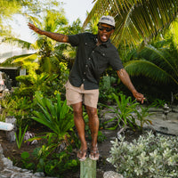 Man wearing black dotted short-sleeve button-up shirt in tropical garden setting