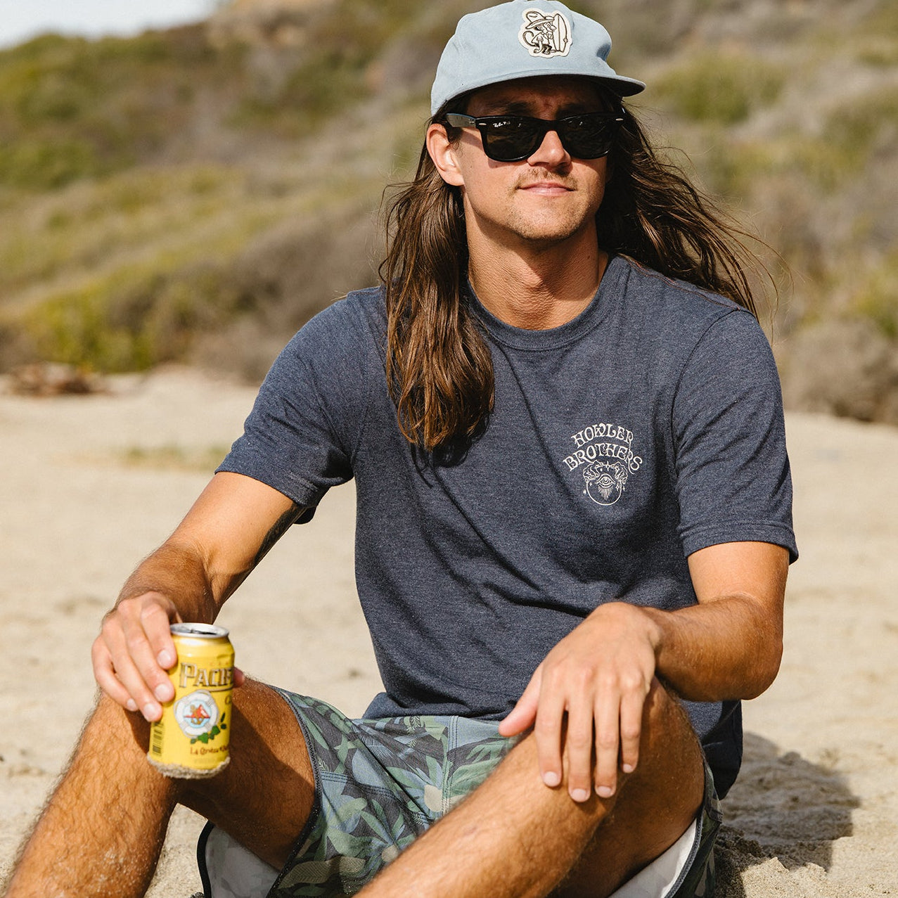 Navy heather t-shirt worn by man sitting on beach holding drink