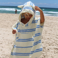 Child wearing hooded towel with blue stripes and ear details on beach