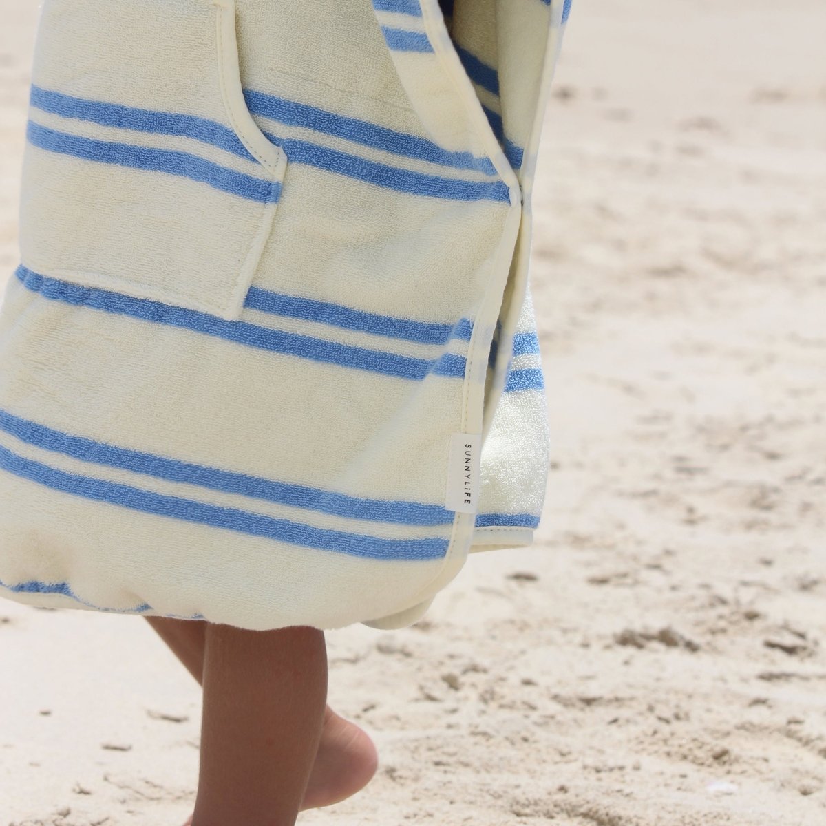 Child wearing striped hooded towel with blue and white pattern on sandy beach