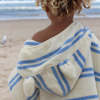 Child wearing blue and white striped hooded towel on beach, back view