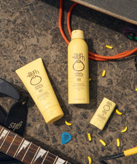 Yellow kids sunscreen stick and lotion tubes with SPF 50 on sandy beach with guitar