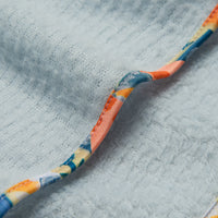 Close-up detail of light blue fleece scarflette showing colorful printed trim binding along the edge