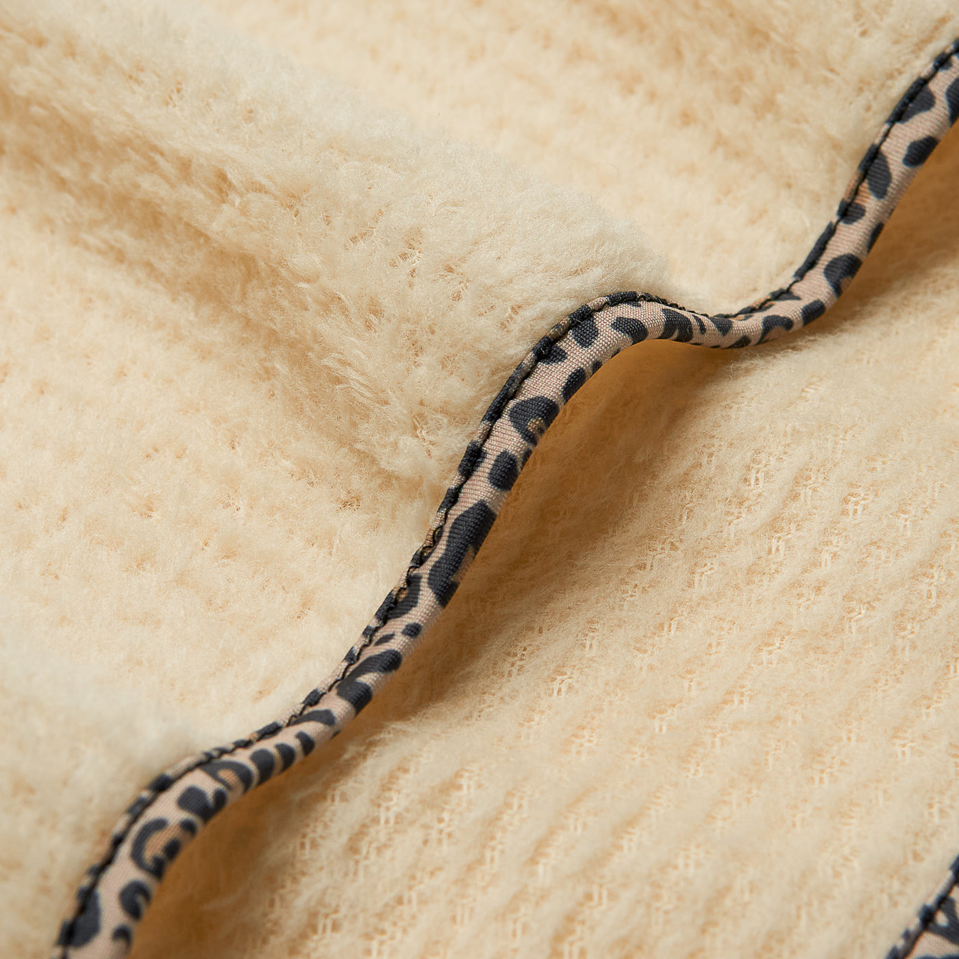 Close-up detail of fleece scarflette showing leopard print trim against cream textured fabric