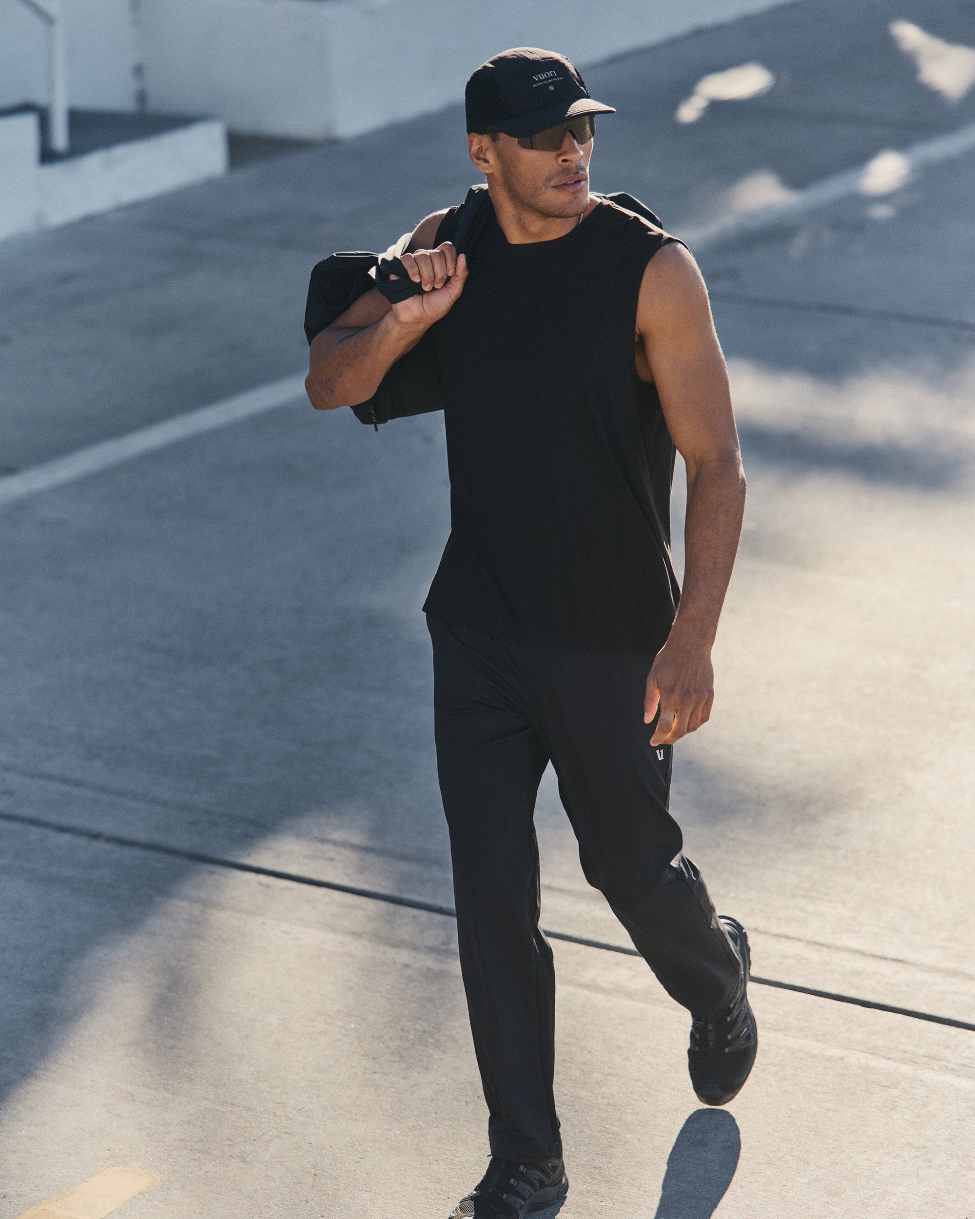 Man walking outdoors in black athletic track pants and sleeveless shirt, carrying bag