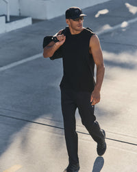 Man walking outdoors in black athletic track pants and sleeveless shirt, carrying bag