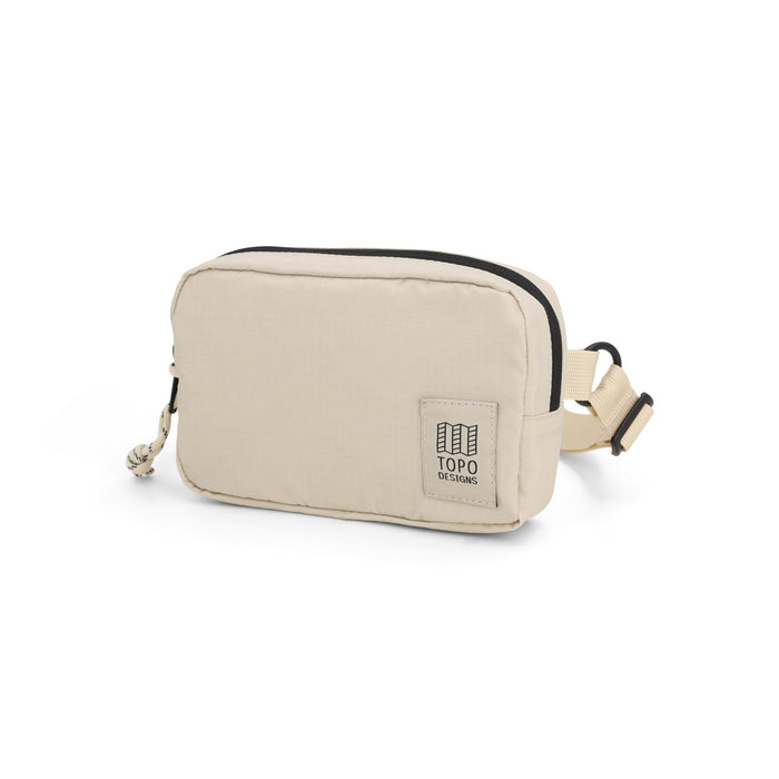 Cream colored belt bag with black zipper trim and adjustable strap, quarter view