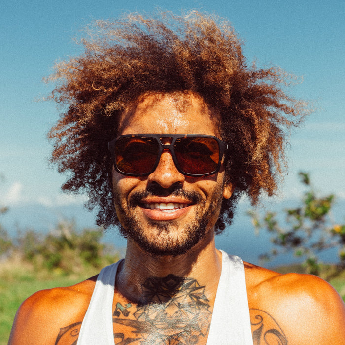 Aviator-style sunglasses with tortoise frame and bronze tinted lenses worn by smiling man outdoors