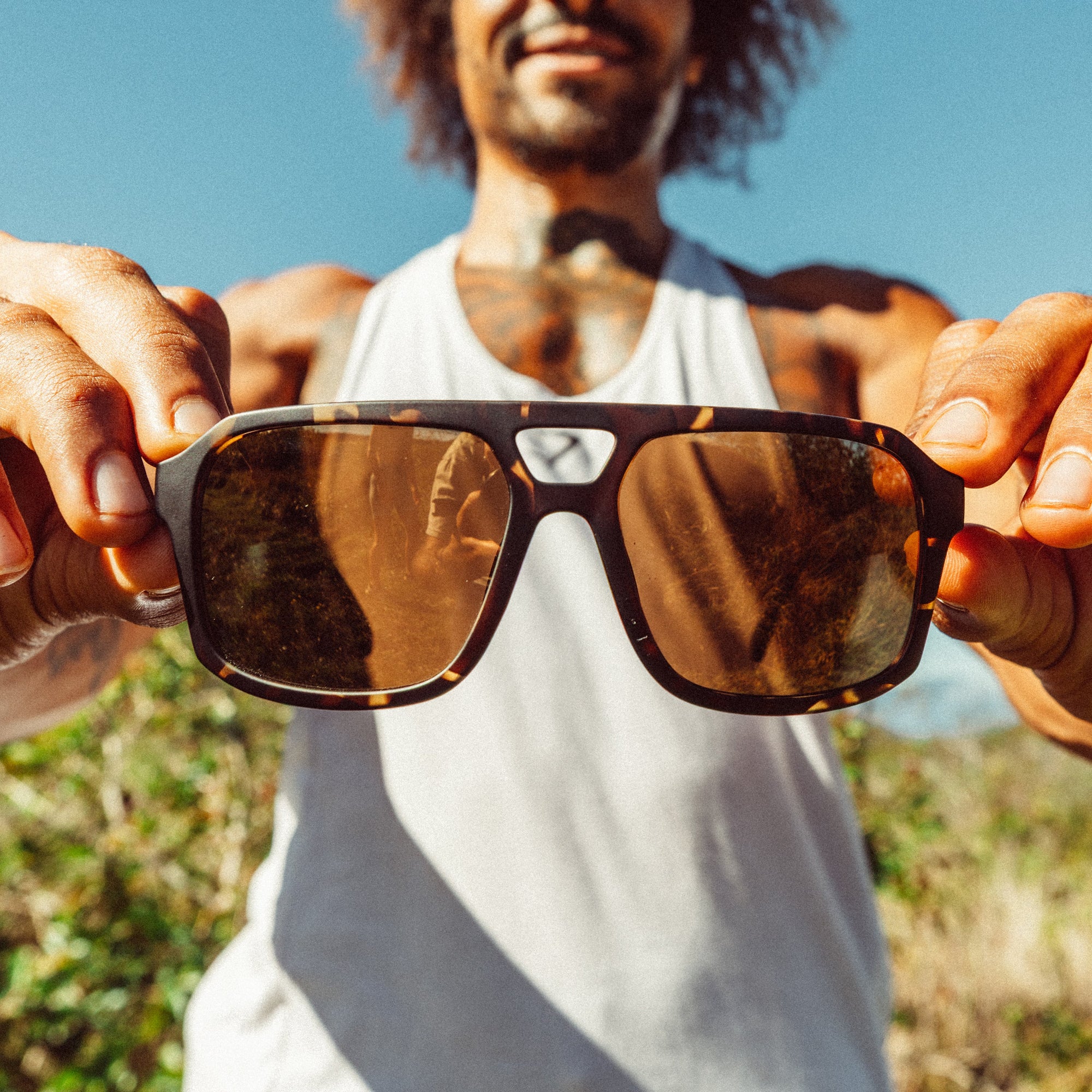 Tortoise shell aviator-style sunglasses with bronze lenses held outward by both hands