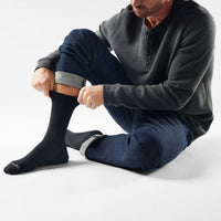 Man sitting on floor pulling on black crew socks with gray cuff detail, jeans rolled up