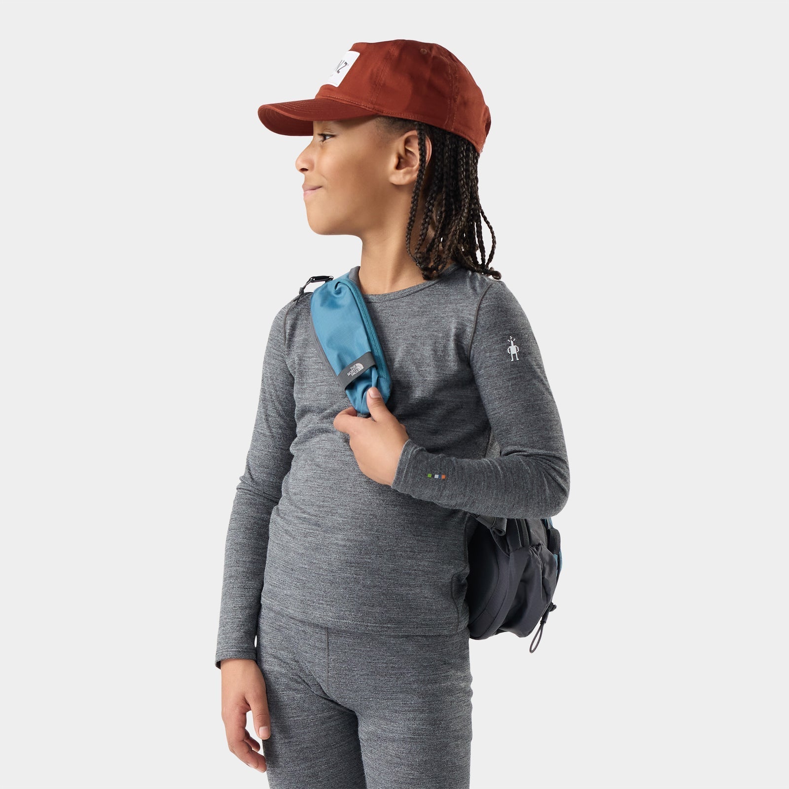 Child wearing long-sleeve gray heather base layer crew with small backpack and red cap