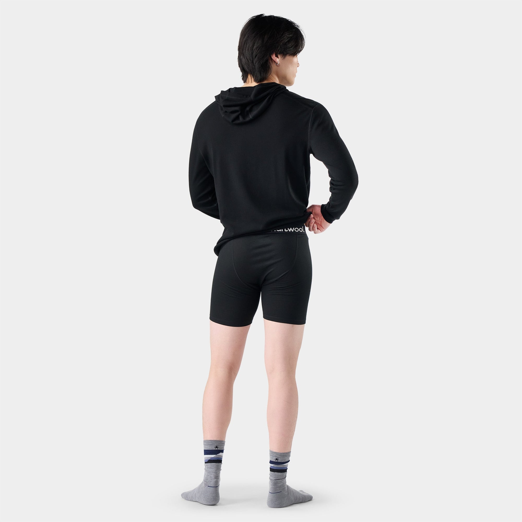 Back view of model wearing black fitted boxer brief shorts with branded waistband and striped socks
