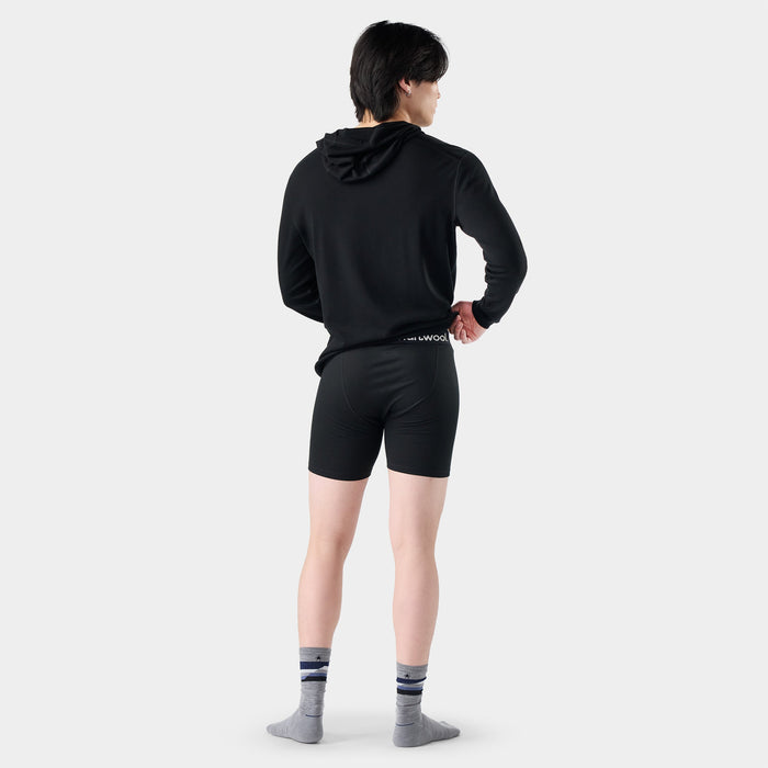 Back view of model wearing black fitted boxer brief shorts with branded waistband and striped socks