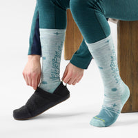 Model putting on tall crew ski socks with floral botanical pattern and cushioned sole, lifestyle shot