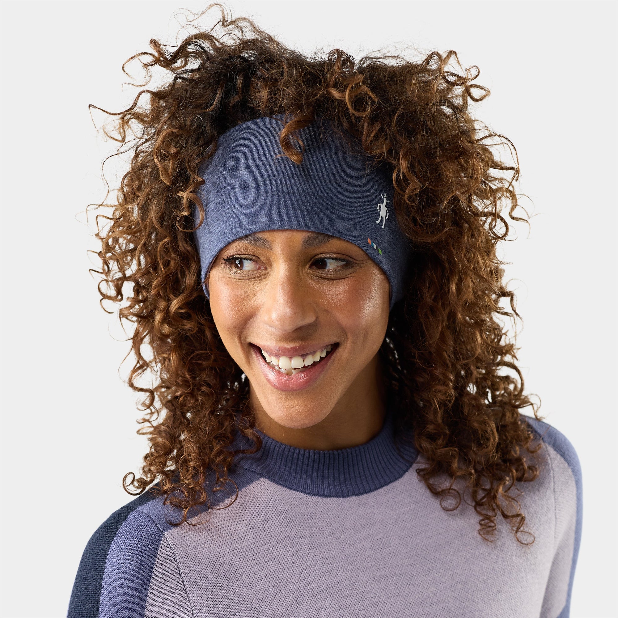 Woman wearing a blue heather merino wool headband with small logo embroidery, curly hair, smiling