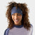 Woman wearing a blue heather merino wool headband with small logo embroidery, curly hair, smiling