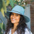 Wide brim woven sun hat in soft teal blue with chin cord, worn by smiling woman outdoors