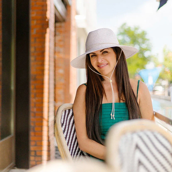 Wide brim sun hat in light beige with chin strap, worn by woman at outdoor café
