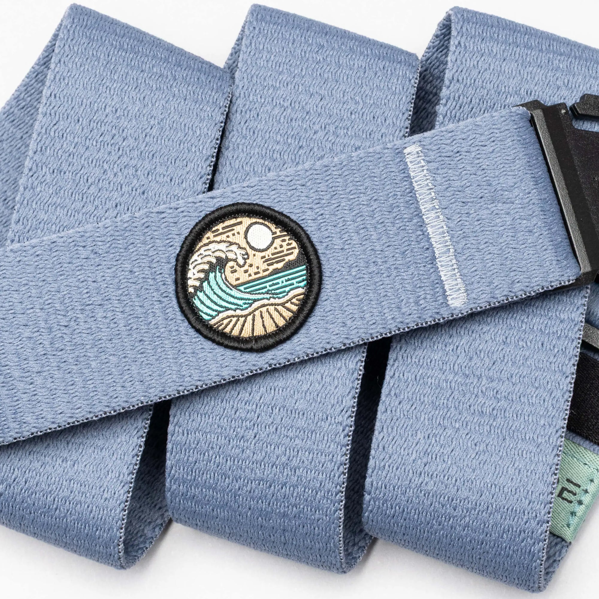 Light blue fabric belt with embroidered circular patch showing waves and landscape design