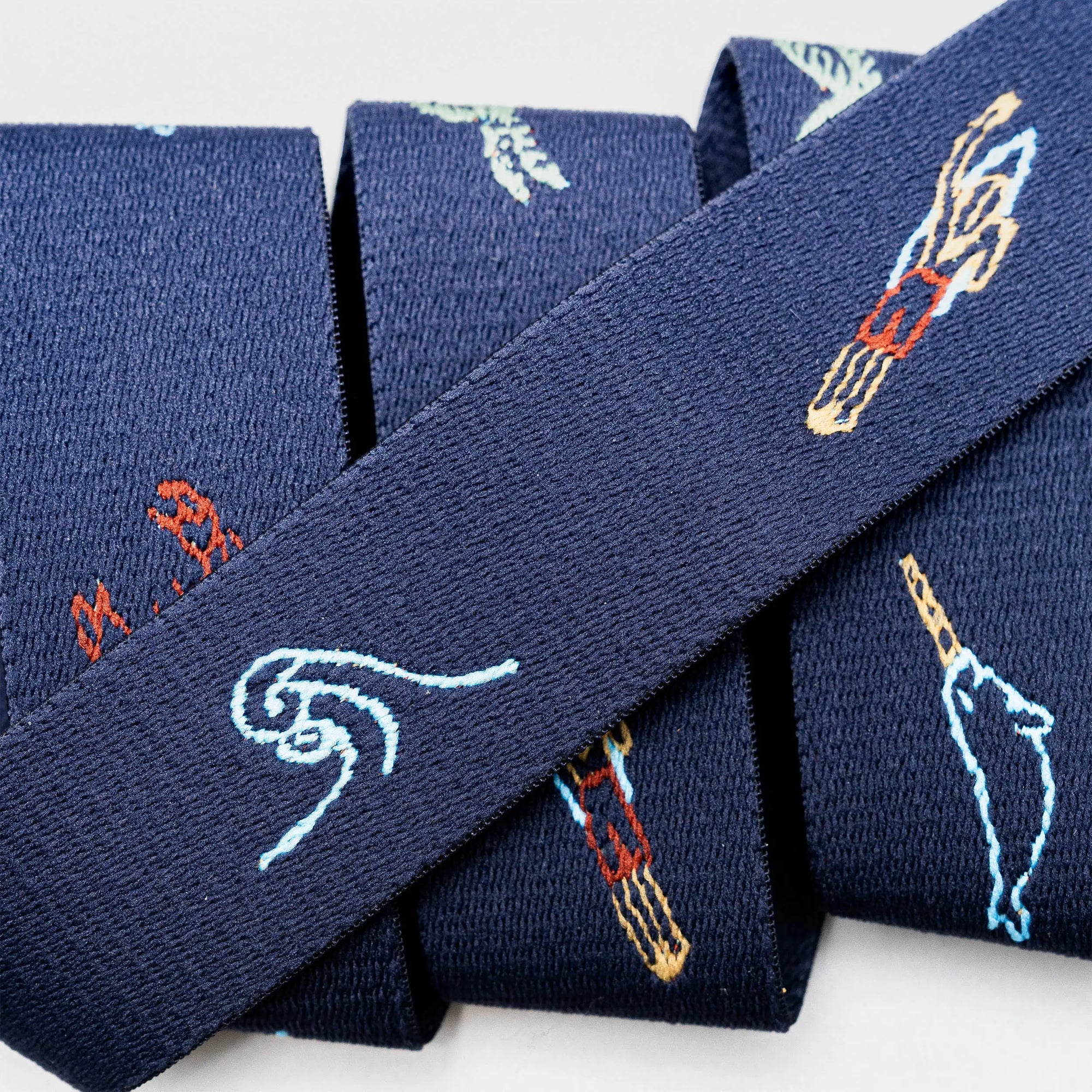 Navy blue fabric belt with colorful embroidered ocean wave and surfboard pattern details