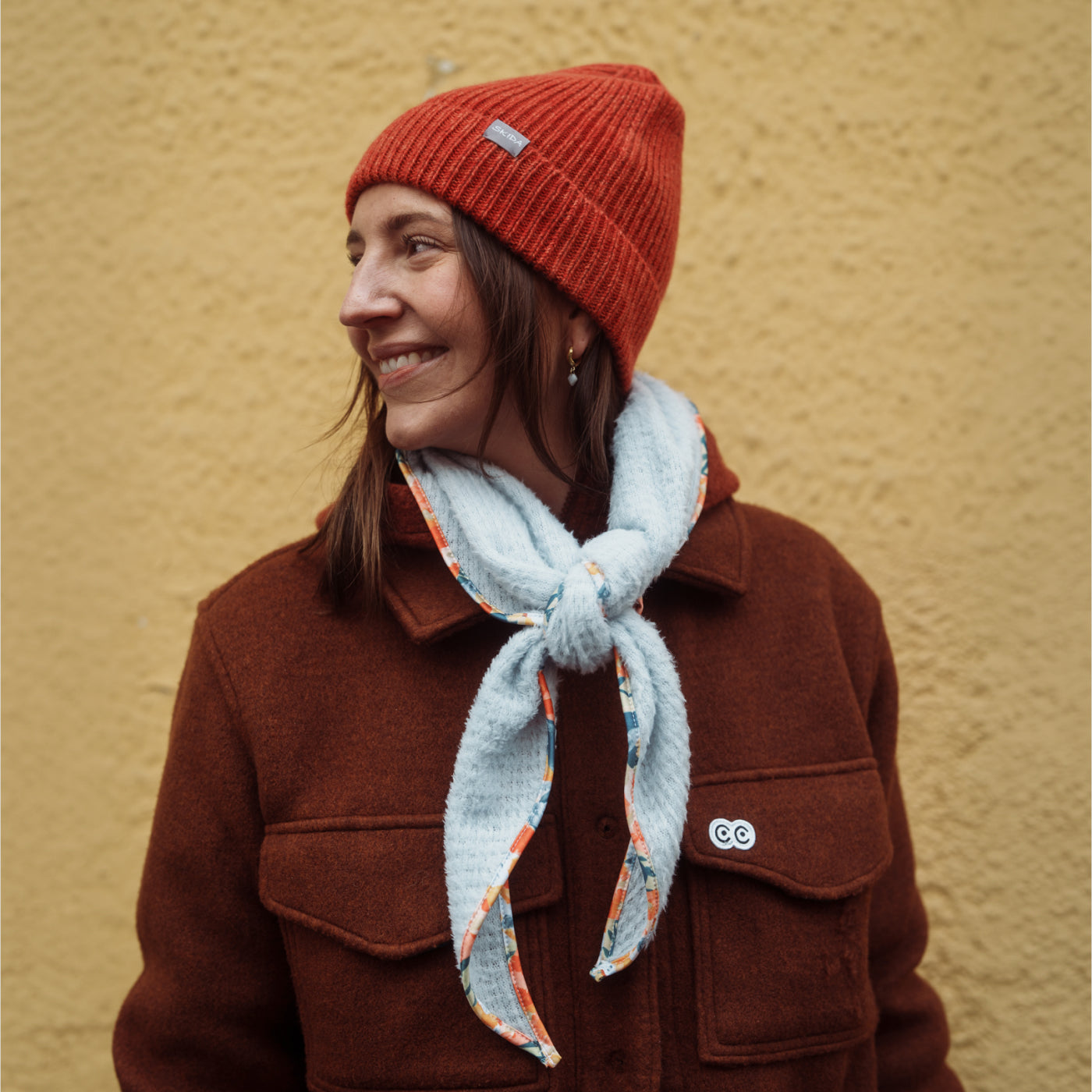 Light blue fleece scarflette with floral trim tied loosely around neck, on-model lifestyle shot