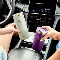 Light green insulated travel mug with straw lid held in car interior
