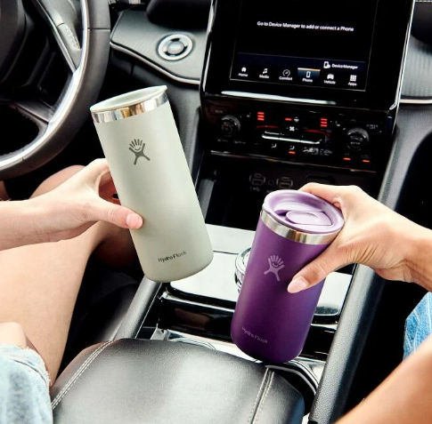 Light green insulated travel mug with straw lid held in car interior