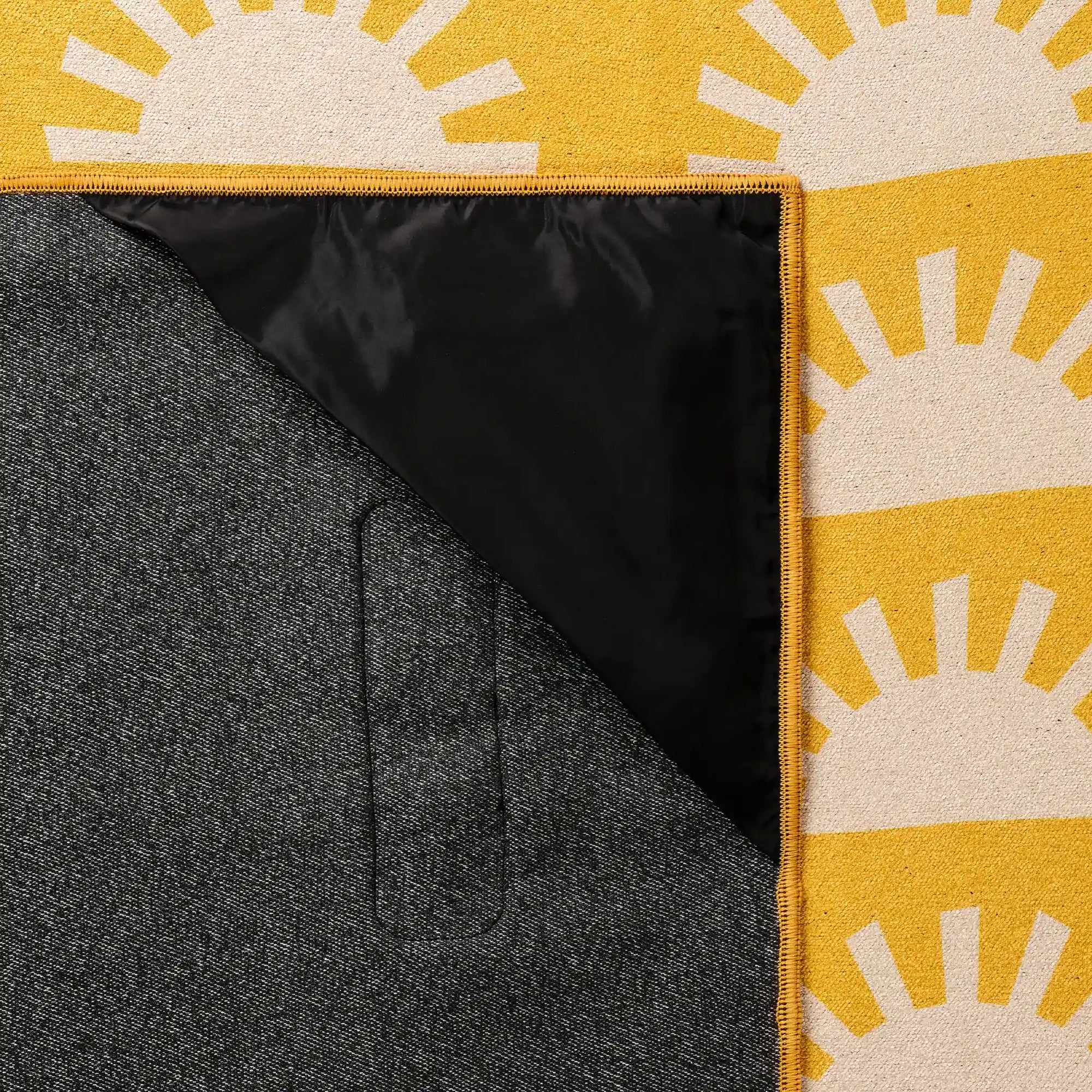 Yellow blanket towel with white sun pattern, showing corner fold revealing black interior lining