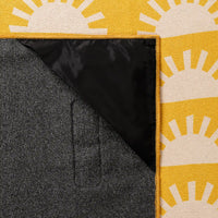 Yellow blanket towel with white sun pattern, showing corner fold revealing black interior lining