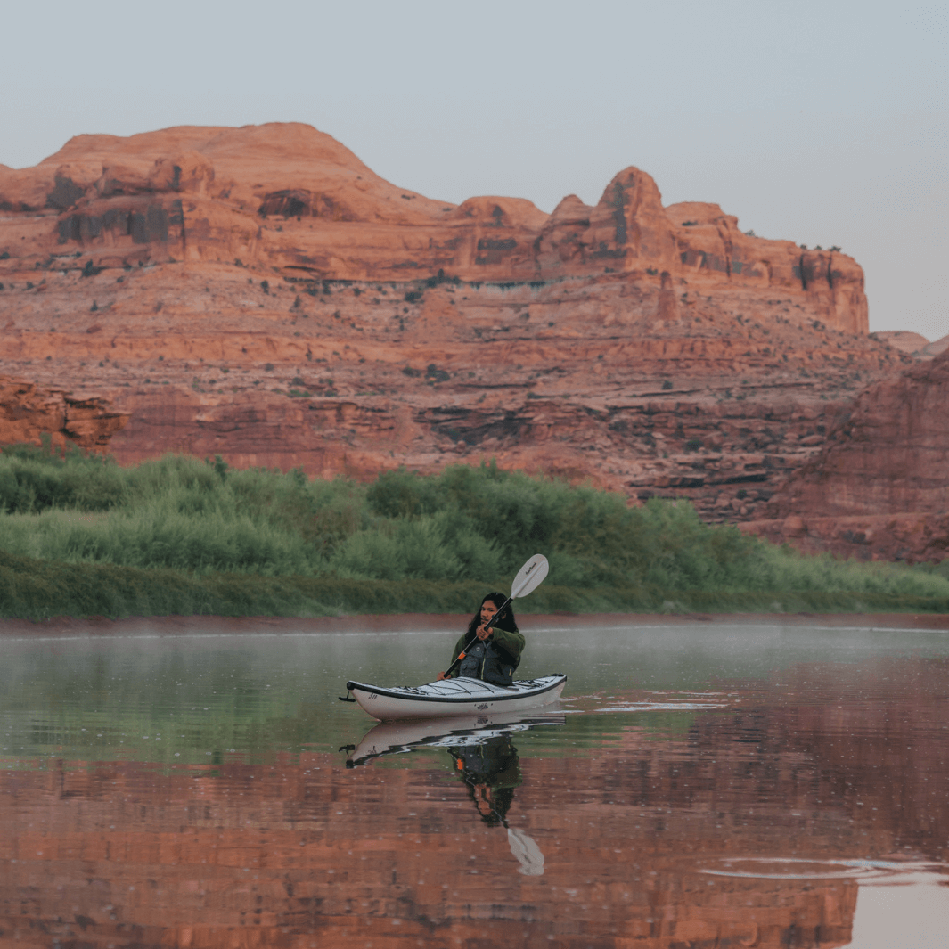 White and gray two-piece kayak paddle being used by person in kayak on calm water