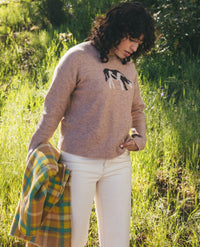 Women's tan crew neck sweater with horse intarsia pattern, styled with cream pants outdoors