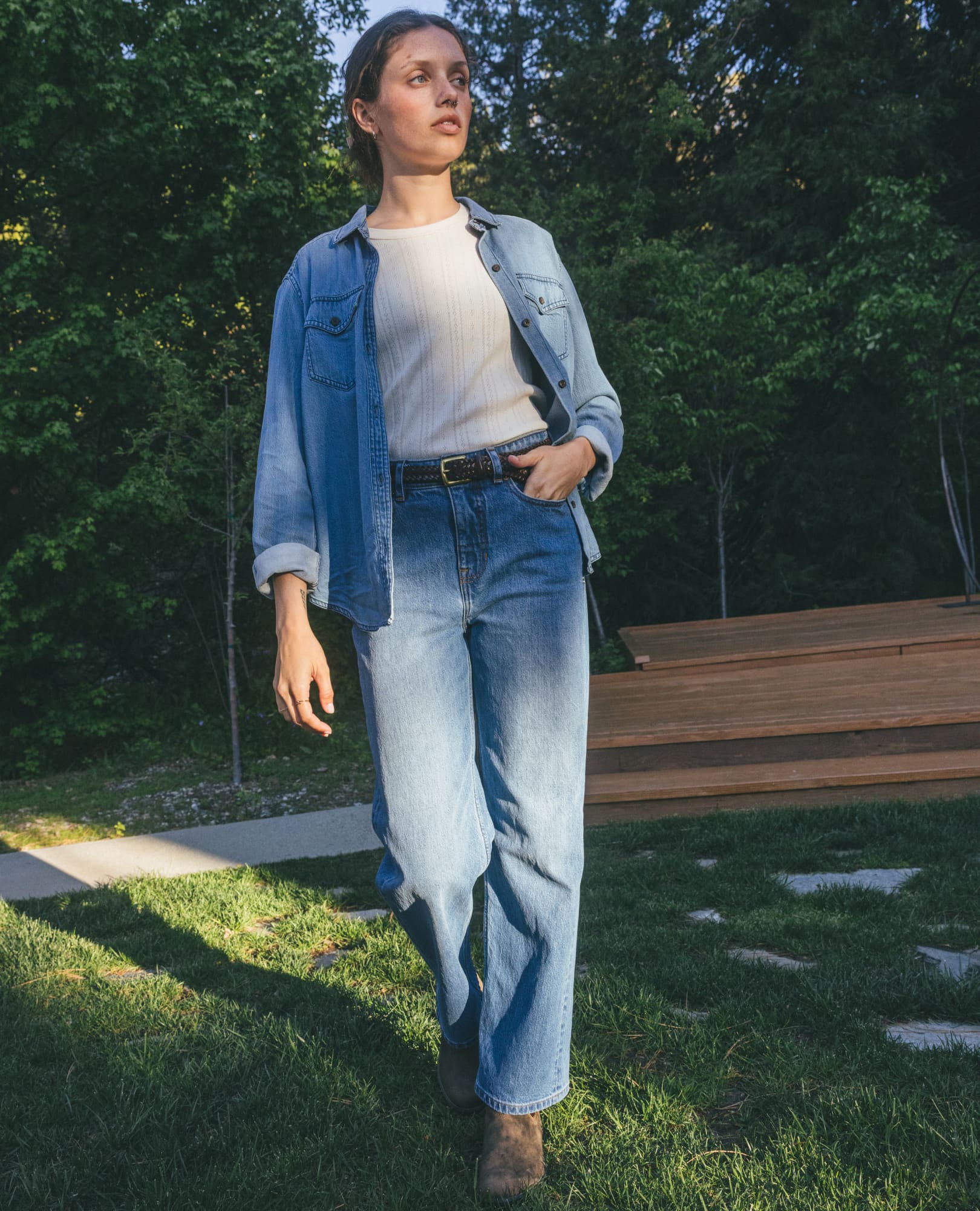Women's light wash denim long-sleeve shirt worn open over white top with jeans, outdoor lifestyle shot
