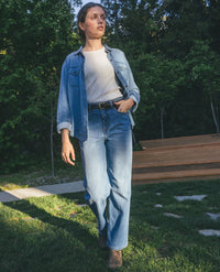 Women's light wash denim long-sleeve shirt worn open over white top with jeans, outdoor lifestyle shot