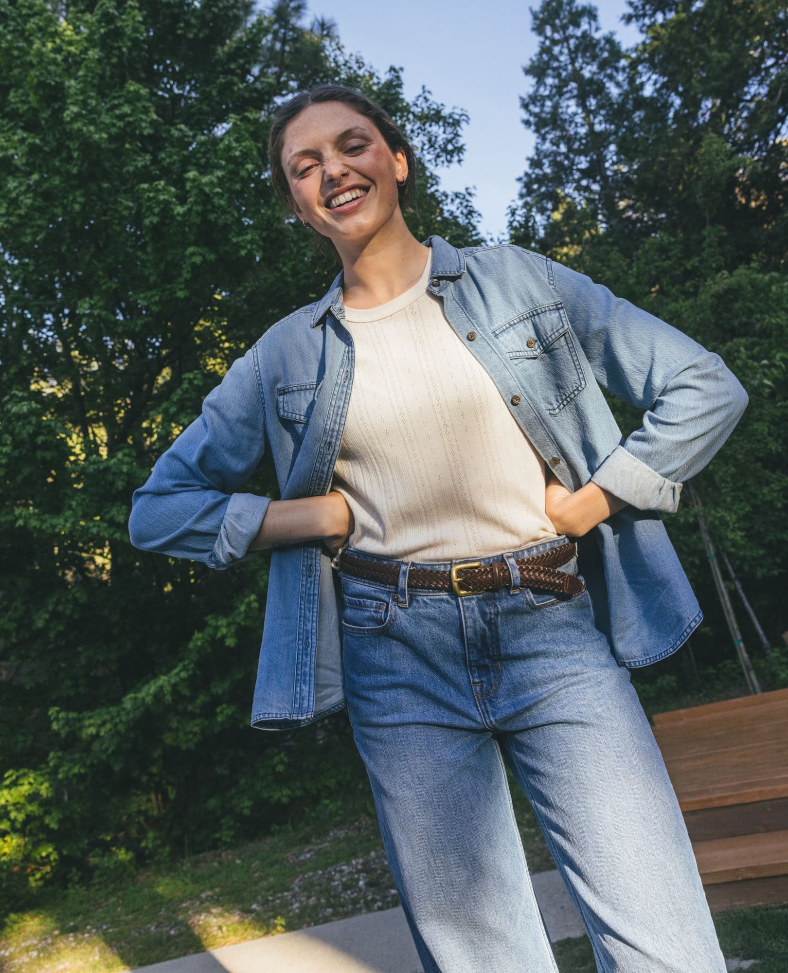 Women's light wash denim long-sleeve shirt worn open over cream top, outdoor lifestyle shot