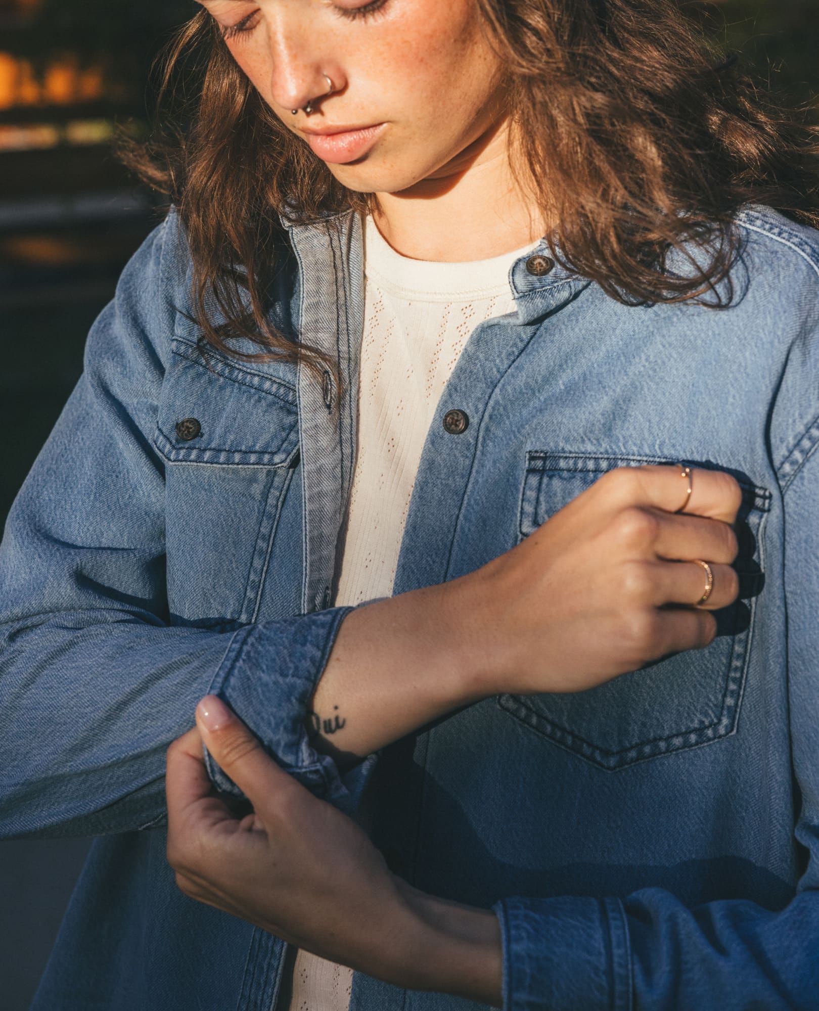 Women's light wash denim long-sleeve shirt, detail view showing chest pocket and wrist tattoo