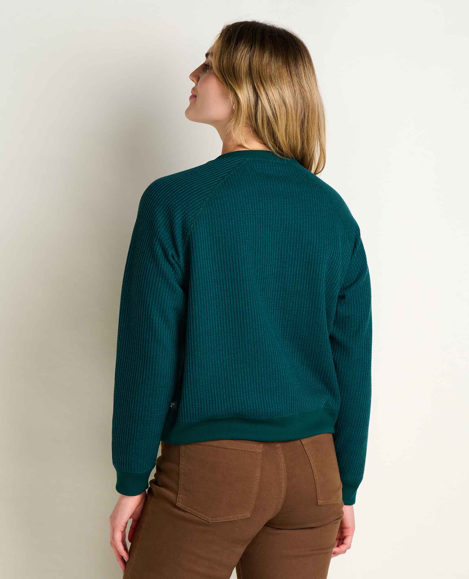 Women's ribbed knit pullover sweater, back view, paired with brown pants