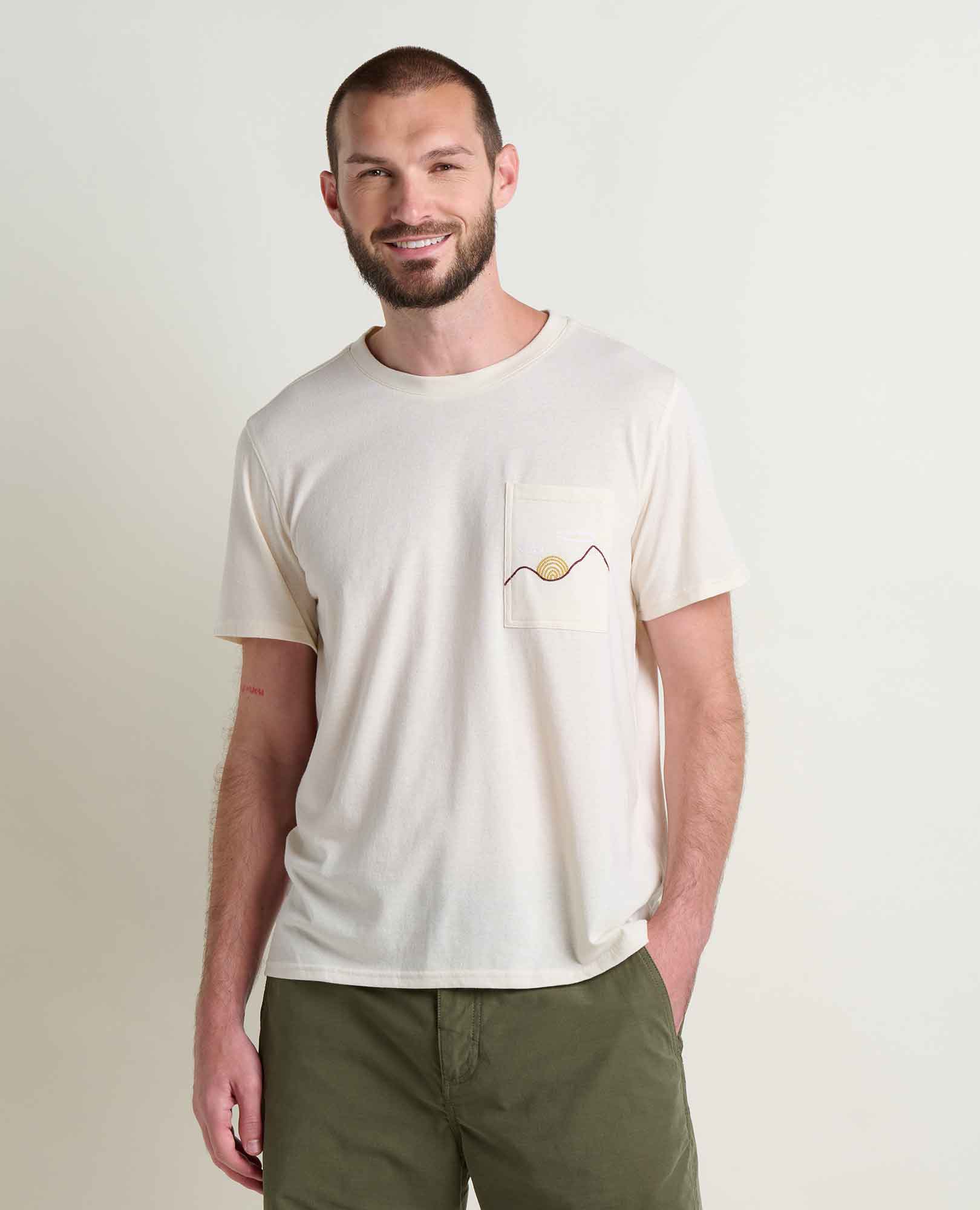 Man wearing cream colored crew neck t-shirt with chest pocket and small embroidered detail