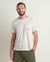 Man wearing cream colored crew neck t-shirt with chest pocket and small embroidered detail