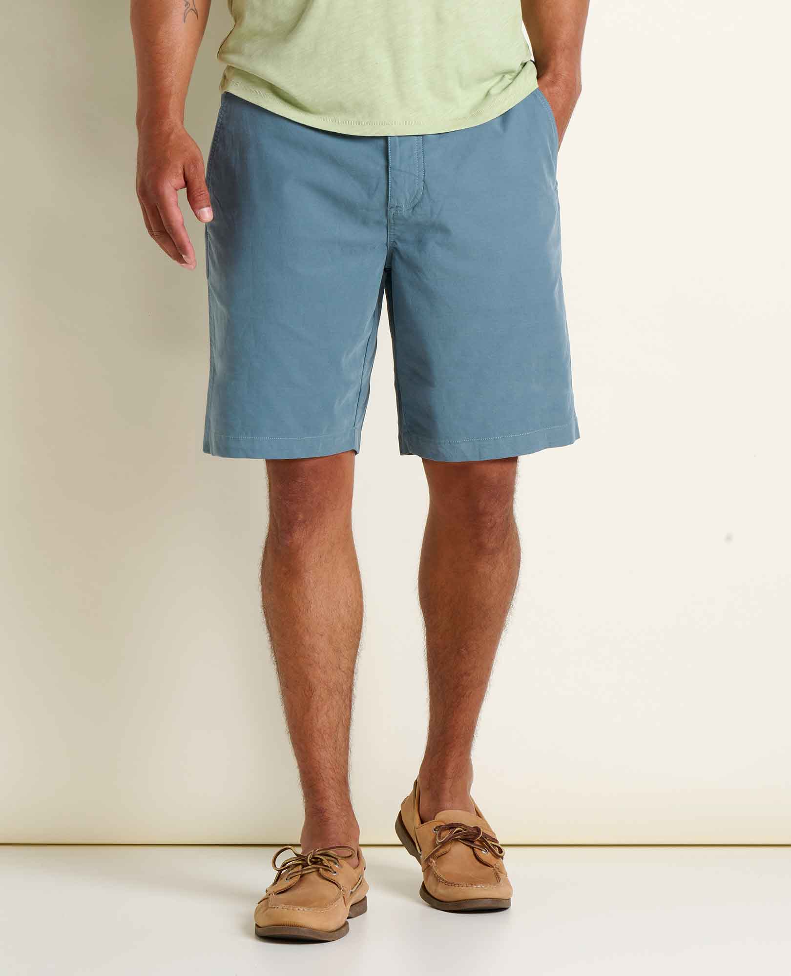 Men's chino shorts in dusty blue worn with boat shoes, front view