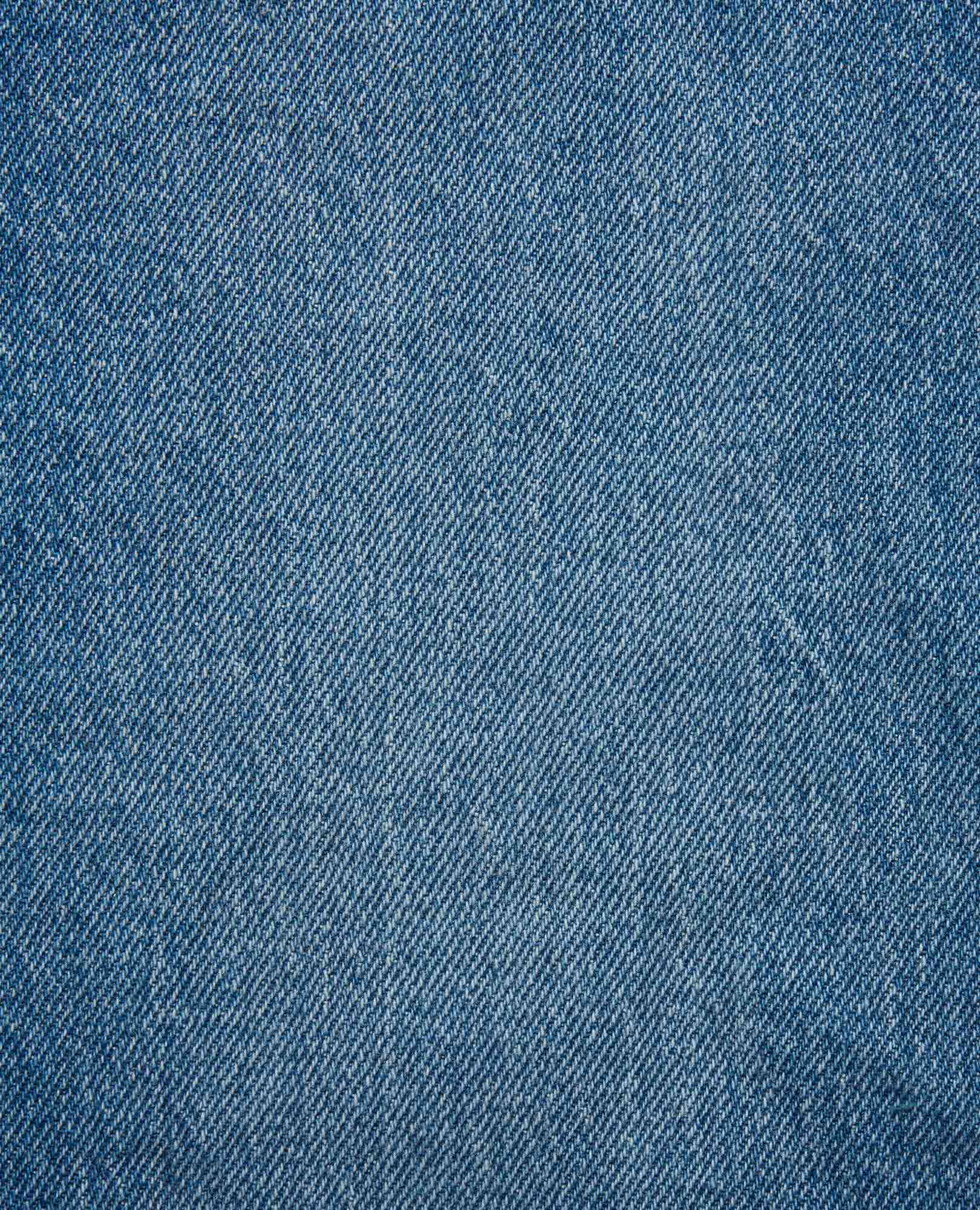 Close-up fabric detail of medium wash blue denim with diagonal twill weave texture
